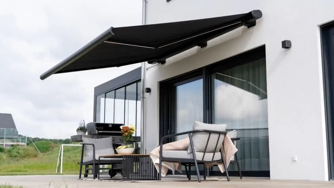 Tenda da sole antracite aperta su una terrazza con poltrone, tavolino e griglia davanti a una casa moderna