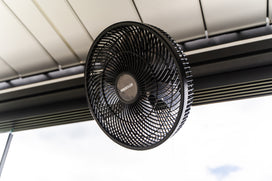 Ventilatore nero con logo PERGOLUX appeso sotto il tetto a lamelle di una pergola bioclimatica, visto dal basso