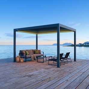 Pergola 4 Pro antracite con luci LED accese su un pontile in legno sul mare al crepuscolo, con divano e sdraio