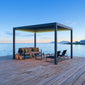 Pergola 4 Pro antracite con luci LED accese su un pontile in legno sul mare al crepuscolo, con divano e sdraio