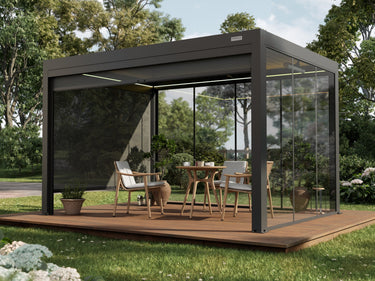 Pergola bioclimatica antracite su una pedana in legno, con pareti in vetro su un lato e un telo oscurante